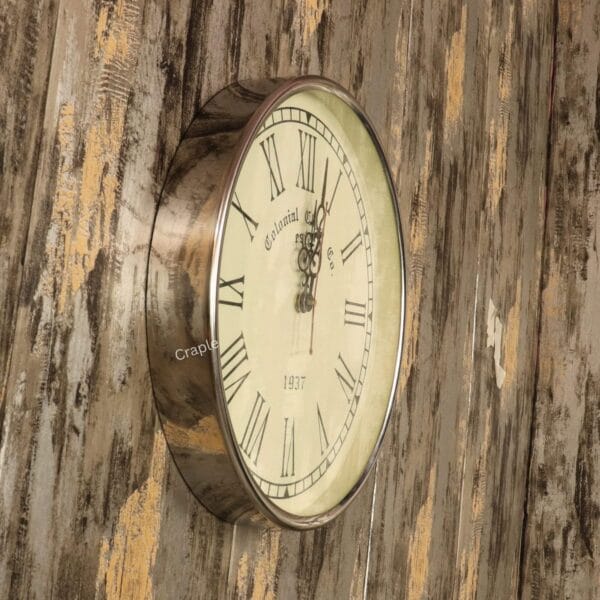 Roman Numeral Silver Steel Wall Clock-2 Angled view of the round silver steel wall clock mounted on a rustic wooden wall.