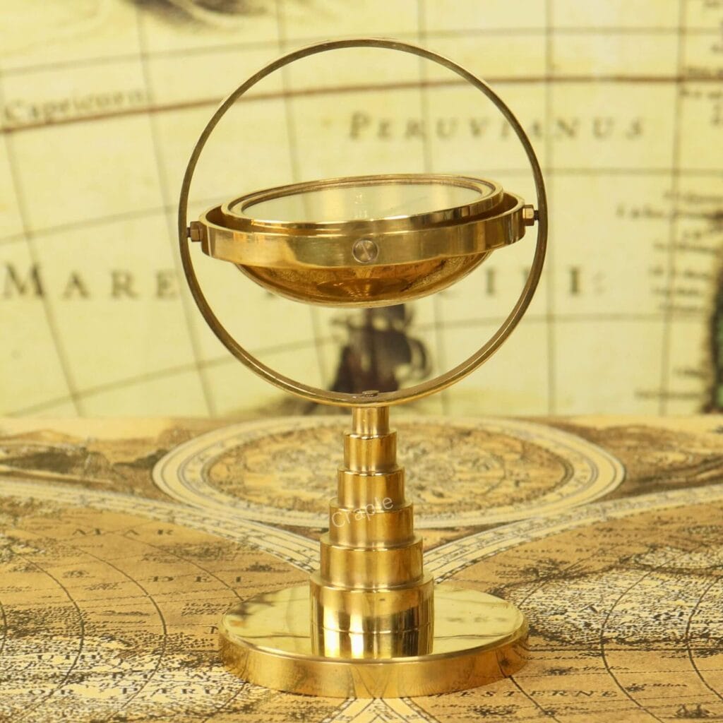Shiny brass desktop gimbal compass on a tiered stand, displayed on a vintage world map.