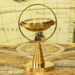 Shiny brass desktop gimbal compass on a tiered stand, displayed on a vintage world map.