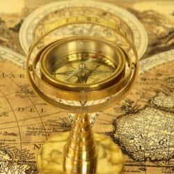 Close-up angled view of a vintage-style brass gimbaled compass, showing the detailed dial and rings.