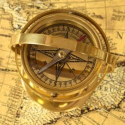 Macro view of the brass compass dial with its magnetic needle, cardinal points, and degree markings.