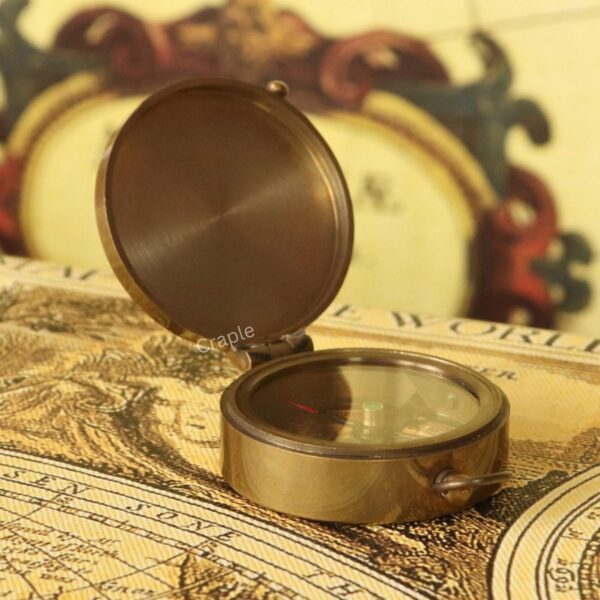 Shiny Brass Pocket Compass with Mirror-1 A closed, shiny brass pocket compass with a glass top revealing the needle, resting on a vintage world map.