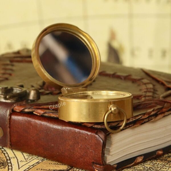 Shiny Brass Pocket Compass with Mirror-2 Side view of the open brass pocket compass on a book, showing the reflection in the lid's integrated mirror.
