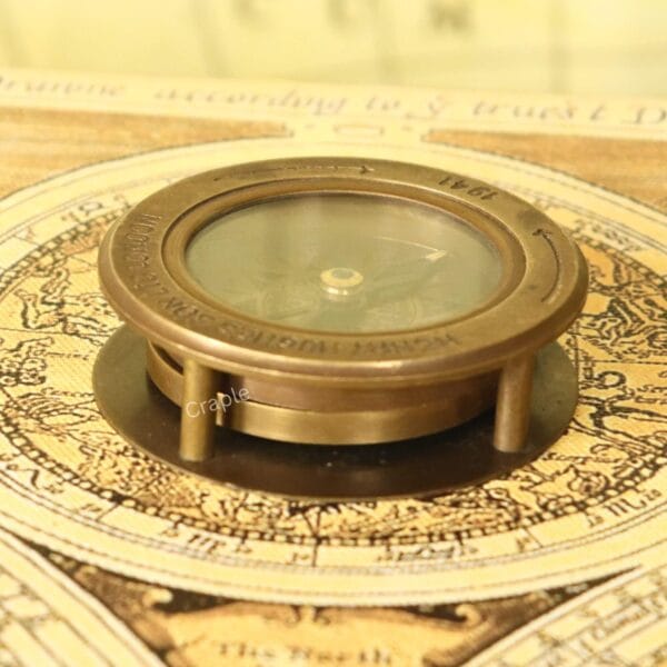 Antique brass desk compass with a built-in magnifier, shown in its closed position on a vintage map.