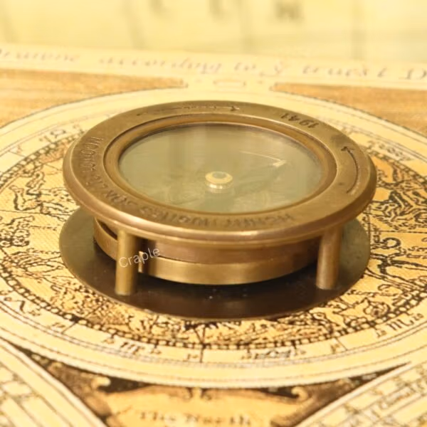Antique brass desk compass with a built-in magnifier, shown in its closed position on a vintage map.