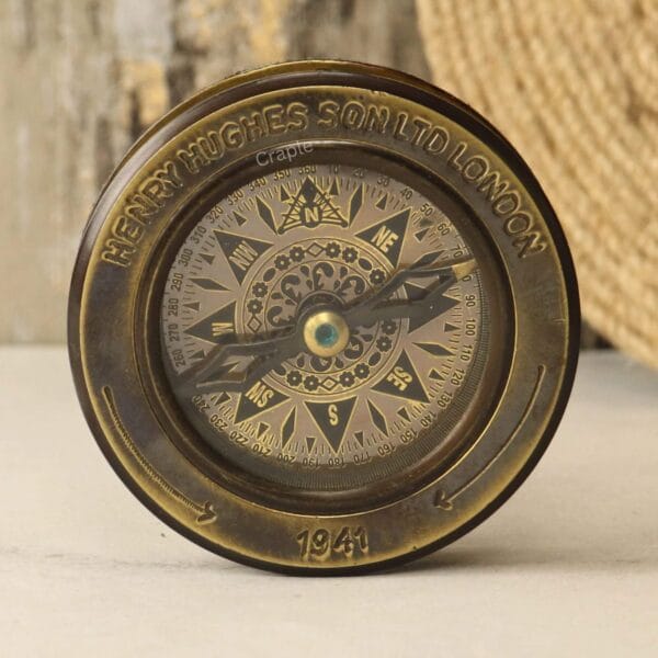 Top-down view of a vintage brass desk compass with a black antique finish and "Henry Hughes London 1941" engraving.