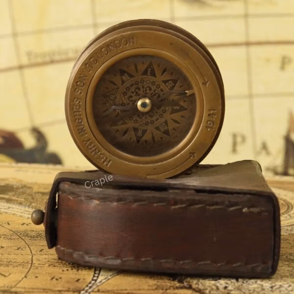 The brass sliding magnifier compass standing upright next to its protective brown leather carrying case.