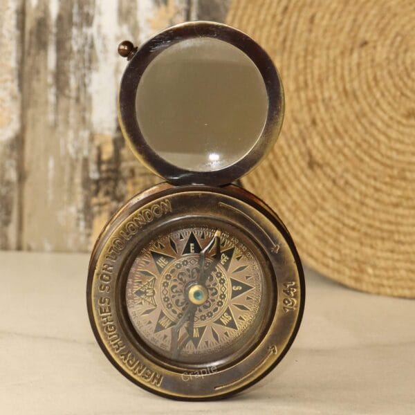 Vintage brass pocket compass with its attached sliding magnifying glass opened to the top.