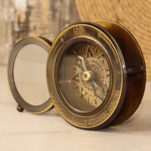 Vintage brass desk compass and paperweight with its sliding magnifier swung open, shown from an angled perspective.