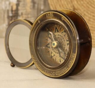 Vintage brass desk compass and paperweight with its sliding magnifier swung open, shown from an angled perspective.