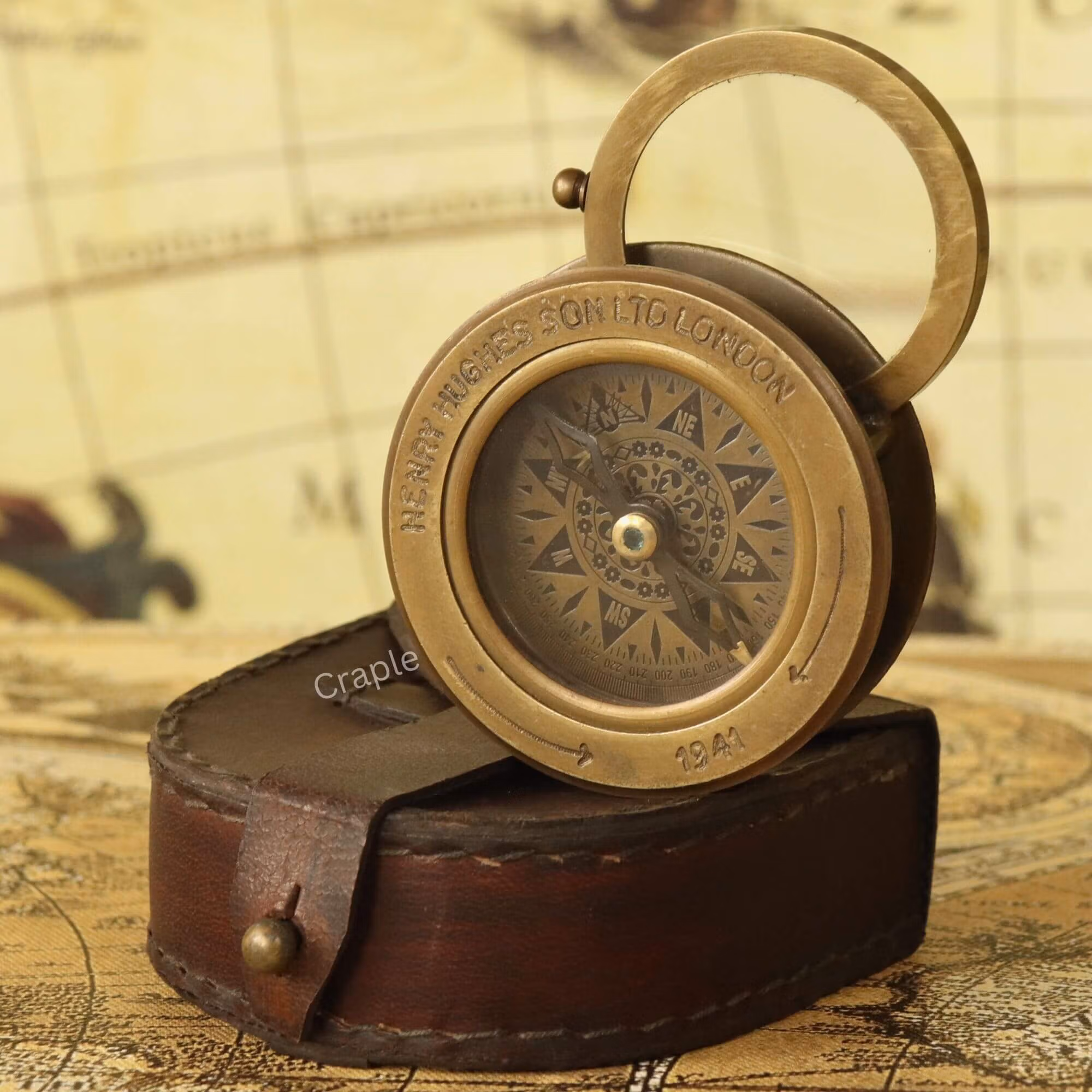 Antique brass sliding desk compass with its flip-up magnifier open, emerging from a stitched leather case.
