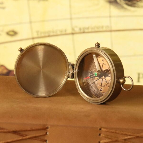 Angled view of the small brass pocket compass with its lid open, resting on a vintage map.