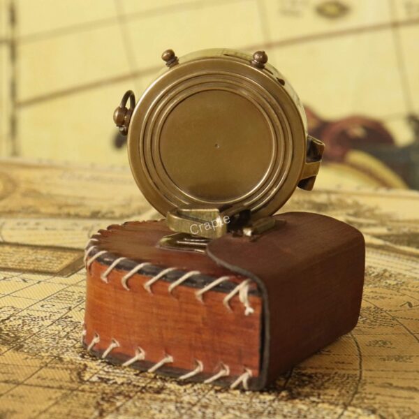 The closed antique brass compass standing next to its protective, stitched leather-style storage pouch.