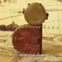 The top of the closed brass pocket compass resting on its rustic storage pouch on a vintage map.