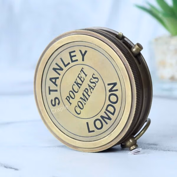 Angled view of the antique brass pocket compass, showing the textured side and hinge mechanism.