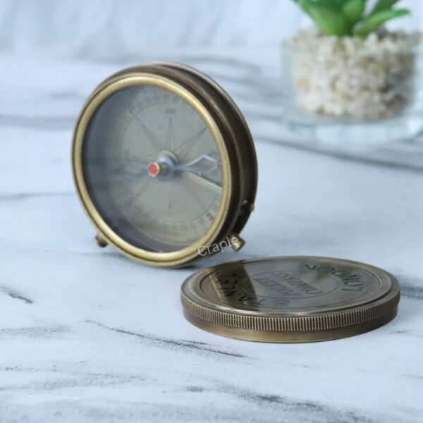 Stanley London Pocket Compass-5 Antique brass pocket compass with its screw-off engraved lid placed beside it on a marble surface.
