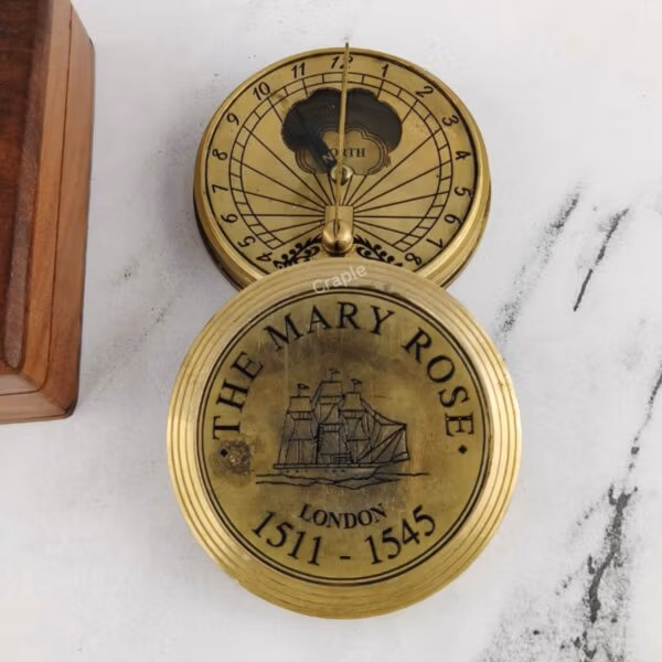Open brass sundial compass with its engraved "The Mary Rose" lid resting beside it.