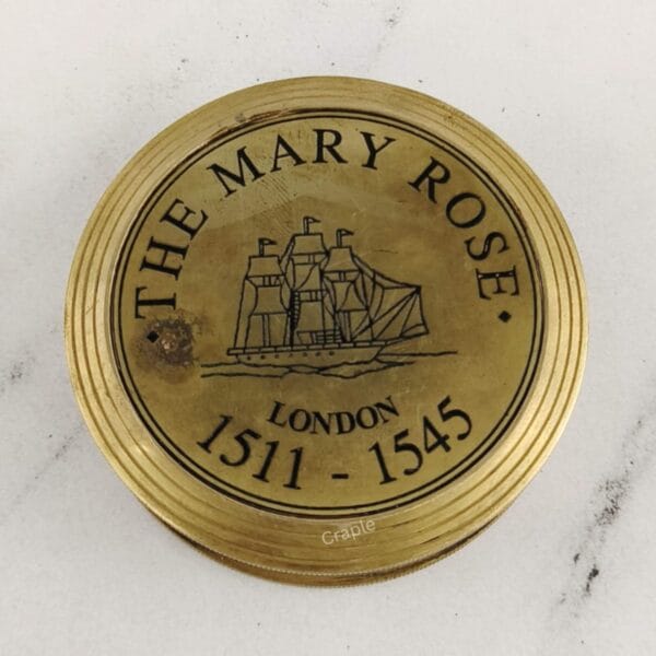 Close-up of the polished brass lid engraved with "THE MARY ROSE LONDON 1511-1545" and a ship illustration.