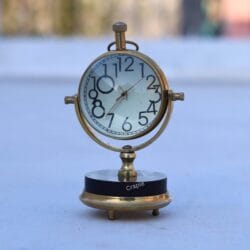 Shiny brass tilting orb desk clock with a black base, featuring a white face with large, classic numbers.