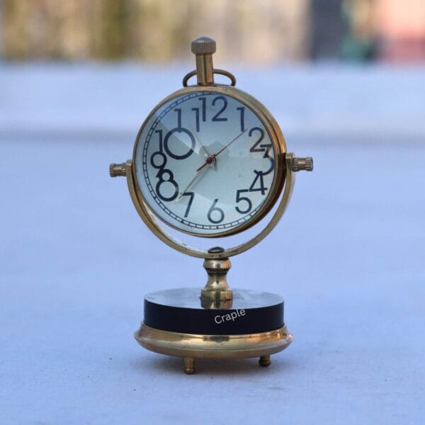 Tilting Orb Shiny Brass Desk Clock-1 Shiny brass tilting orb desk clock with a black base, featuring a white face with large, classic numbers.