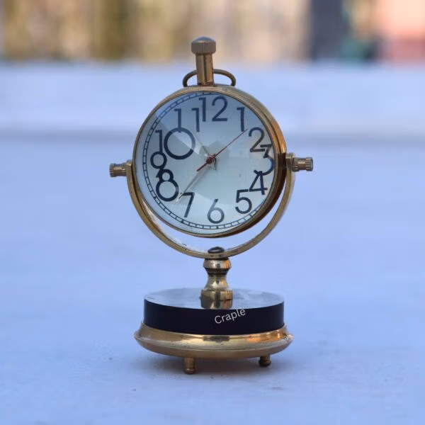 Shiny brass tilting orb desk clock with a black base, featuring a white face with large, classic numbers.