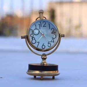 Angled view of the vintage brass orb clock, showing its gimbal-style tilting frame and round, sturdy base.