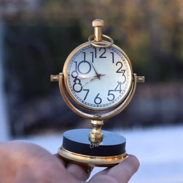 A person holding the brass orb tabletop clock to demonstrate its size and polished finish.