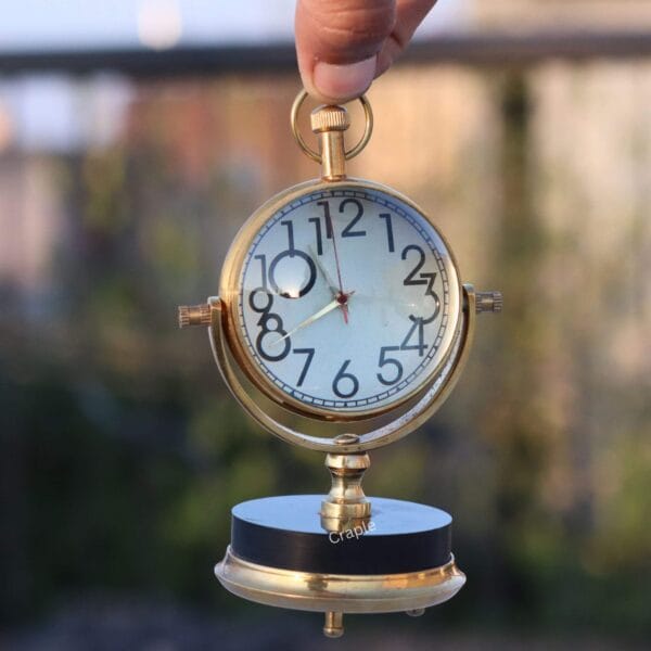 Tilting Orb Shiny Brass Desk Clock-5 The tilting brass desk clock held up, showing a clear view of the clock face and its gimbal frame.