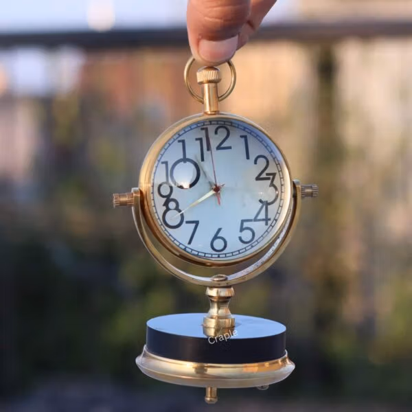 The tilting brass desk clock held up, showing a clear view of the clock face and its gimbal frame.