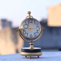 The vintage brass orb desk clock sitting on a ledge outdoors, showing its polished finish in natural light.