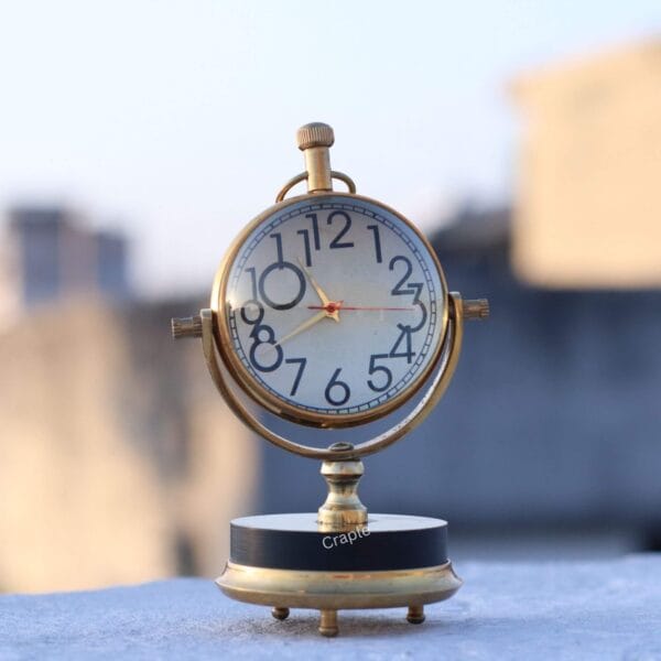 Tilting Orb Shiny Brass Desk Clock-6 The vintage brass orb desk clock sitting on a ledge outdoors, showing its polished finish in natural light.