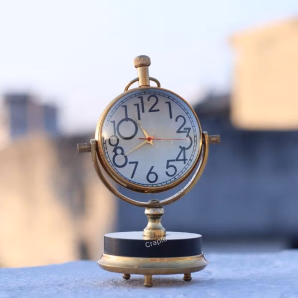 The vintage brass orb desk clock sitting on a ledge outdoors, showing its polished finish in natural light.