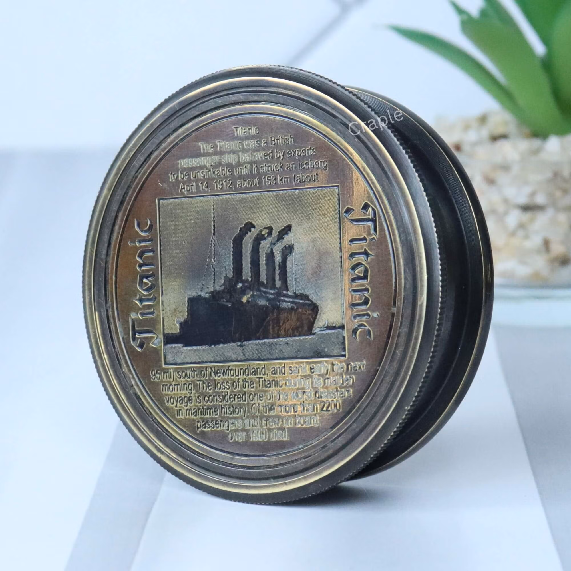Antique black brass pocket compass with an embossed Titanic lid, shown at an angle to display its depth and detail.