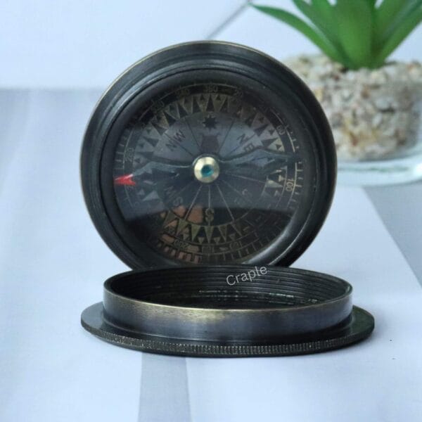 The two-part black antique brass compass, with the Titanic-embossed lid resting next to the open compass base.