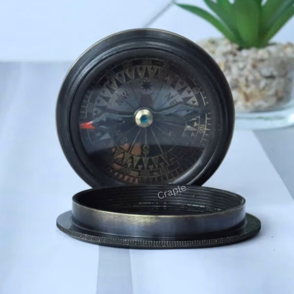 The two-part black antique brass compass, with the Titanic-embossed lid resting next to the open compass base.