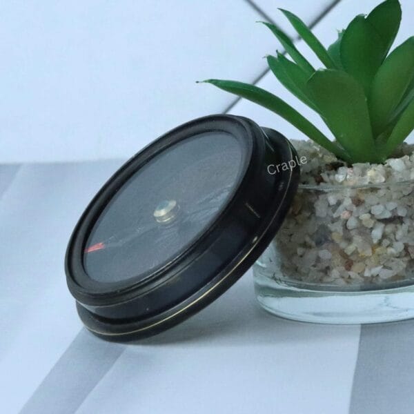 A tilted, angled view of the closed Titanic pocket compass, highlighting its round shape and antique finish.