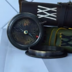 The open antique black compass displayed with its lid, next to a vintage-style leather pouch.