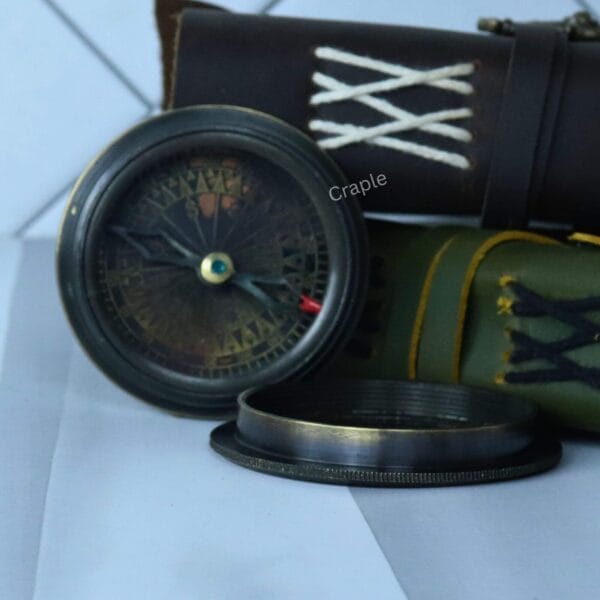 The open antique black compass displayed with its lid, next to a vintage-style leather pouch.