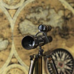 Close-up of the eyepiece and finder scope on the antique brass telescope, set against a vintage map background.