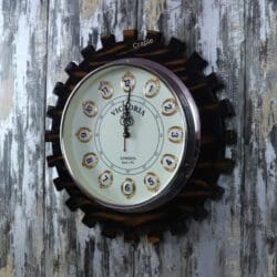 Close-up of the "Victoria London" clock face with ornate hands, set within the dark, gear-toothed wooden frame.