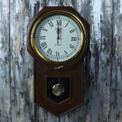 Vintage wooden pendulum wall clock with a golden brass-faced bezel, a white dial with Roman numerals, and a visible pendulum.