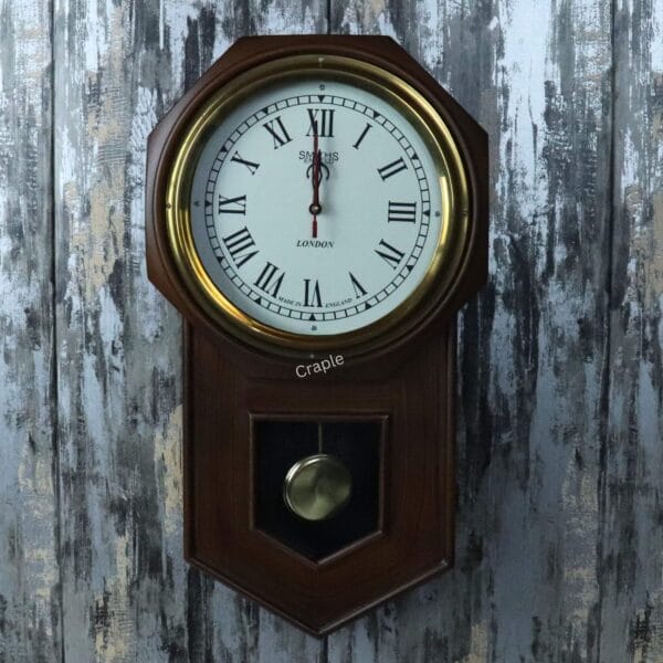Vintage wooden pendulum wall clock with a golden brass-faced bezel, a white dial with Roman numerals, and a visible pendulum.