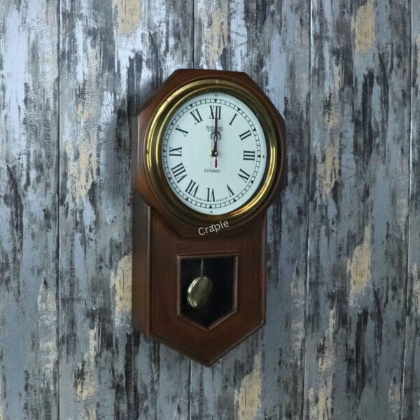Vintage wooden pendulum wall clock with a golden brass-faced bezel, a white dial with Roman numerals, and a visible pendulum.