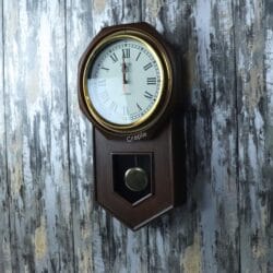 Close-up of the brass-faced pendulum clock, focusing on the round clock face and the octagonal wooden frame.