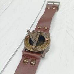 Vintage brass sundial compass with its full brown leather strap and buckle laid flat to show its complete design.
