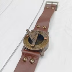 Vintage brass sundial compass with its full brown leather strap and buckle laid flat to show its complete design.