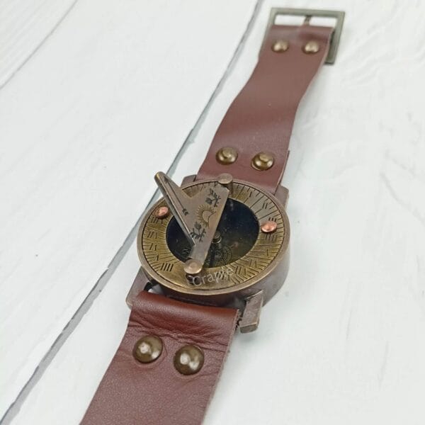 Vintage brass sundial compass with its full brown leather strap and buckle laid flat to show its complete design.