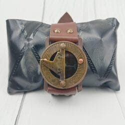 The vintage brass and leather wrist sundial displayed on a black cushion, perfect as a gift item.