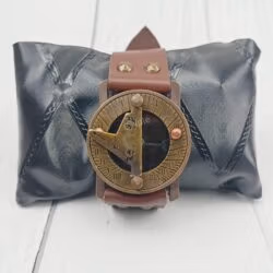 The vintage brass and leather wrist sundial displayed on a black cushion, perfect as a gift item.