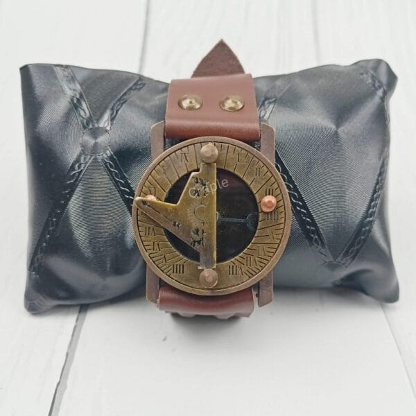The vintage brass and leather wrist sundial displayed on a black cushion, perfect as a gift item.
